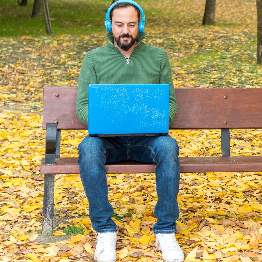 A student with headphones and laptop sitting on an outside bench